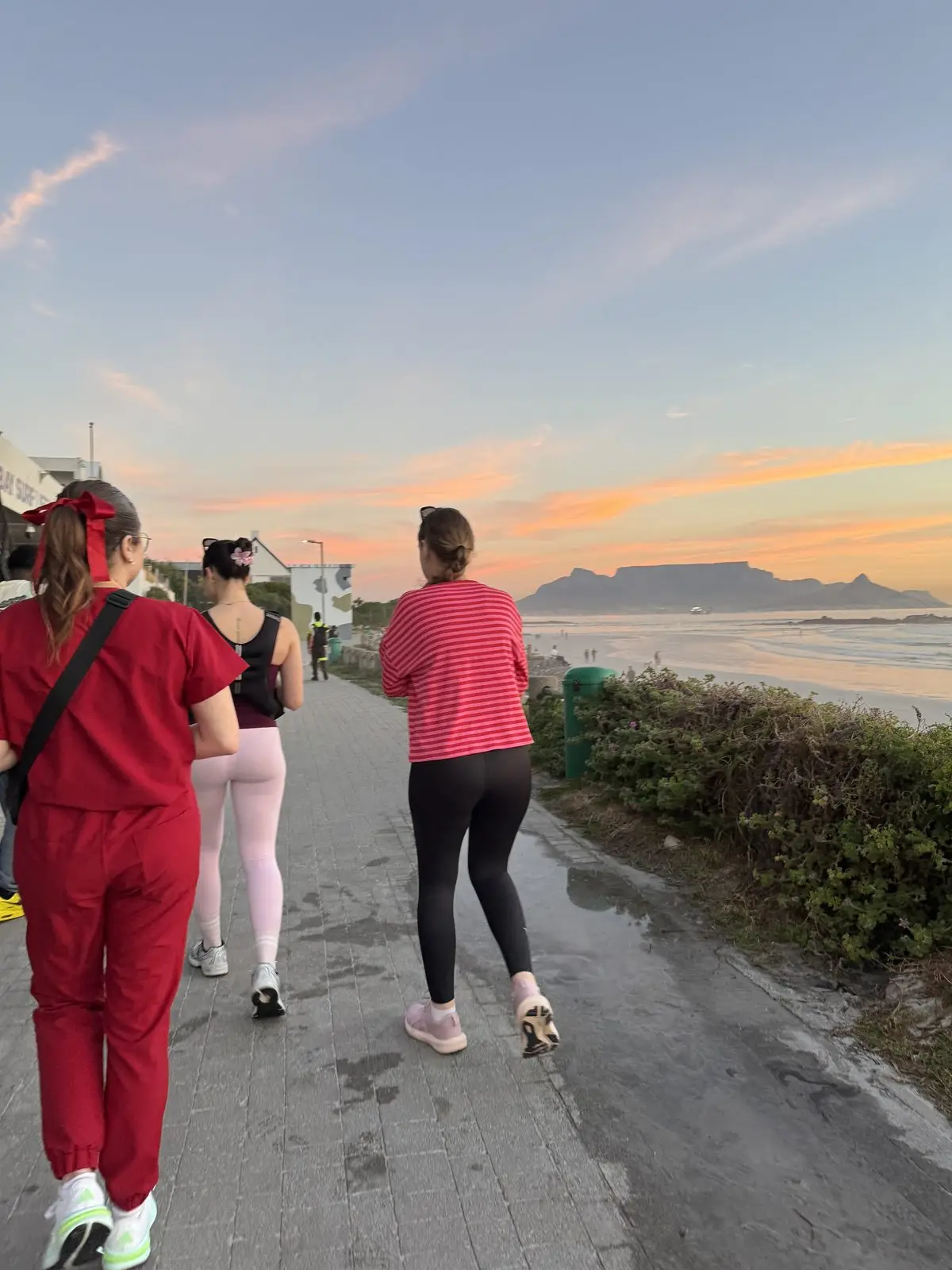 Three women walking a beachfront path at sunset with Table Mountain behind