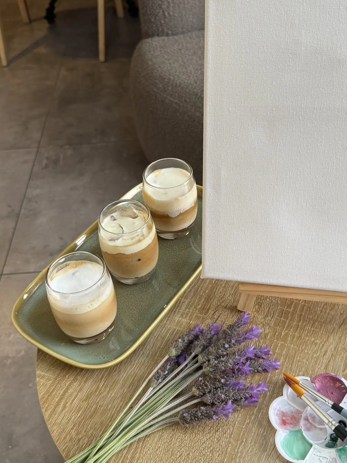 Iced coffees on a tray beside a blank canvas, lavender and a paint palette