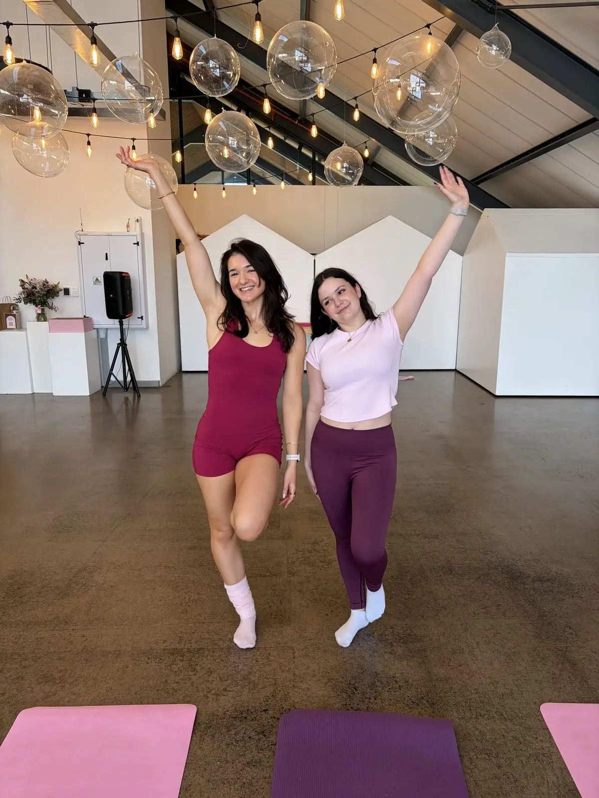 Two women posing with arms raised in a studio hung with globe lights
